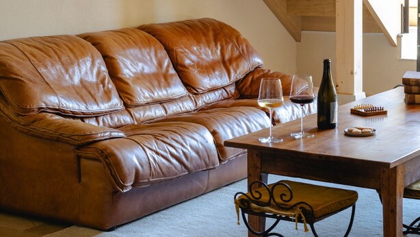 A living room with a brown leather sofa, a wooden coffee table, a bench, and a staircase. - AUBERGE DE MARIGNA (Marigna-sur-Valouse)