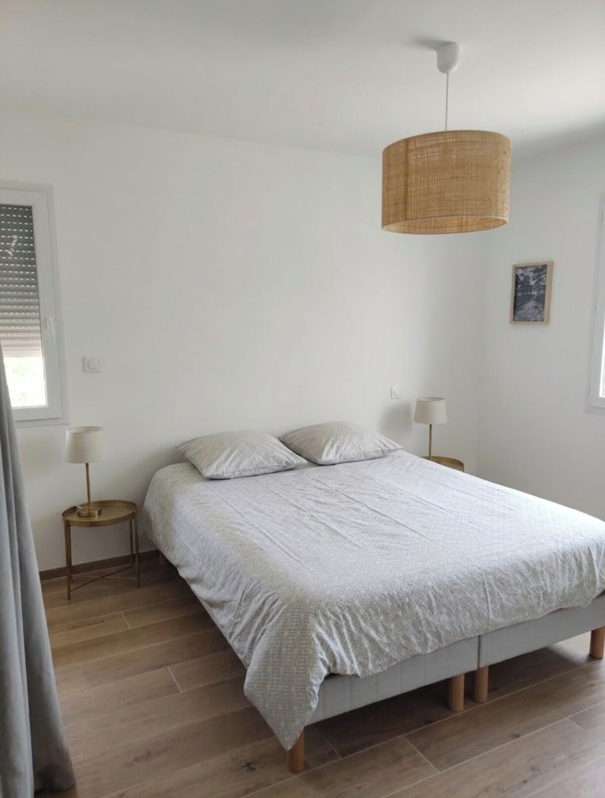 A bedroom with a bed, bedside lamps, a hanging light fixture, and a framed picture on the wall.