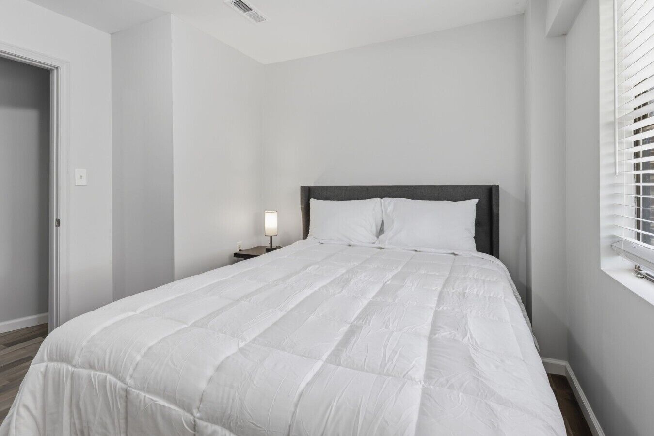 Een slaapkamer met een bed, nachtkastje en een raam met zonwering.
