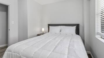 Een slaapkamer met een bed, nachtkastje en een raam met zonwering.