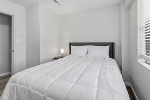 A bedroom with a bed, bedside table, and a window with blinds.