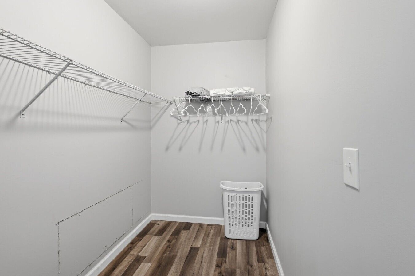 A laundry room with a metal drying rack, a white laundry basket, and a wall-mounted towel rack.