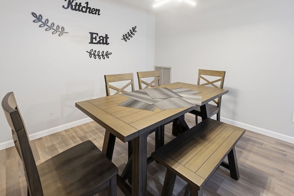 Un coin repas avec une table et des chaises en bois, un mur décoratif orné de motifs et une grille d’aération.