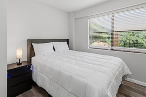 Une chambre à coucher avec un lit, une table de chevet, une lampe et une fenêtre avec des stores.