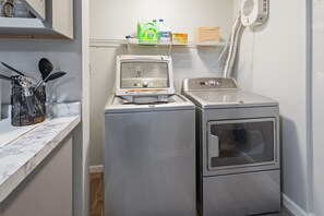 A laundry area with a washing machine, dryer, and a shelf with cleaning supplies.