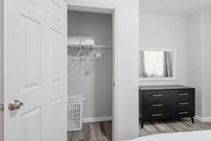 Une chambre avec une porte blanche, une commode noire dotée de poignées dorées, un miroir au-dessus de la commode et un panier à linge.