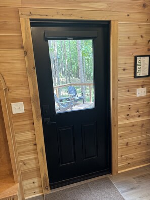 A black door with a window leading to an outdoor deck with chairs and a table. - The Redbud Tiny House at Cyprus Trail (Rockbridge)