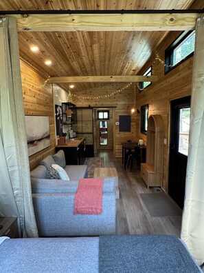 A cozy cabin interior with a sofa, dining table, and kitchen area. - The Redbud Tiny House at Cyprus Trail (Rockbridge)