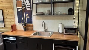 Een moderne keuken met een houten aanrechtblad, zwarte kastjes, een ingebouwde oven en een wandplank met glazen.