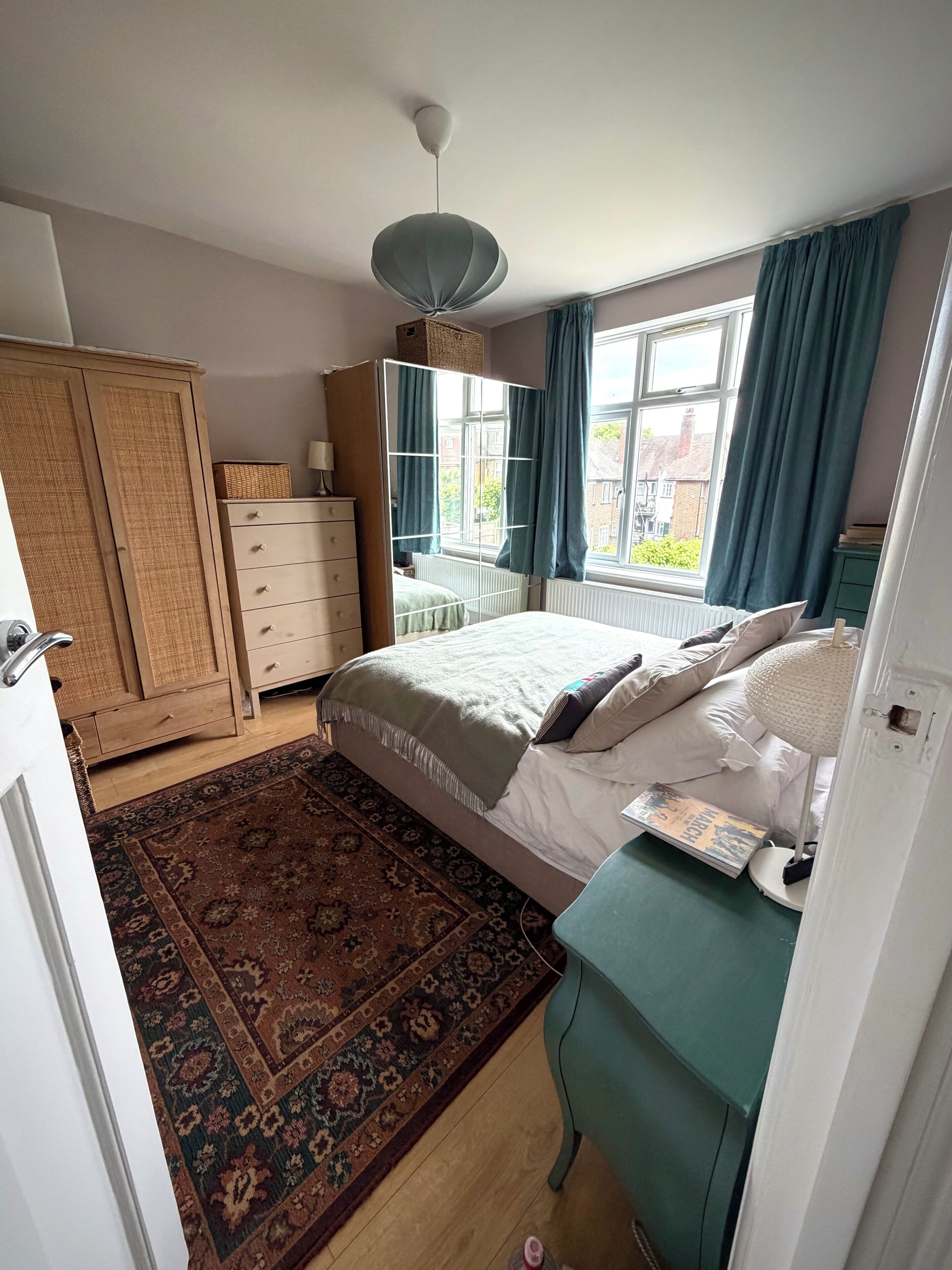 A bedroom with a bed, dresser, wardrobe, and a window with curtains.