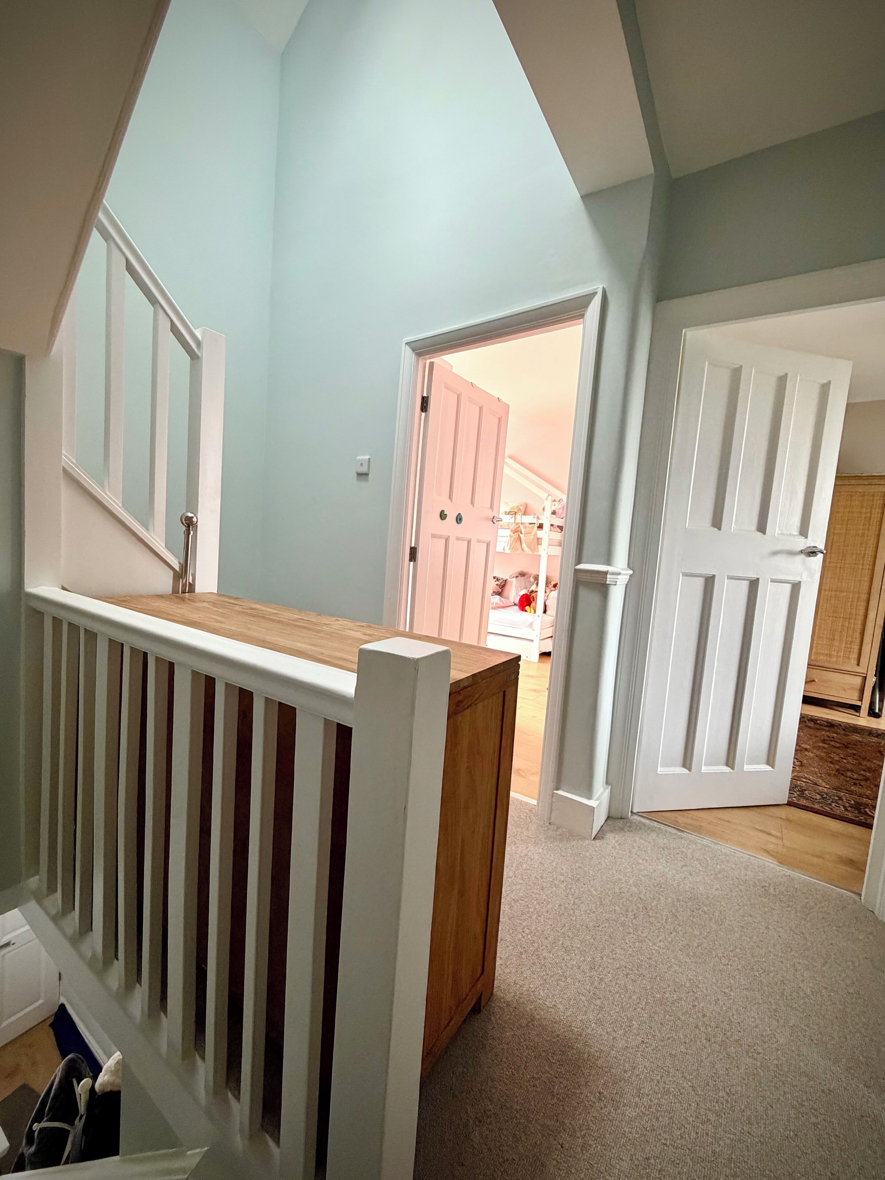 A room with a sloped ceiling, a wooden bench, and a white door leading to another room.