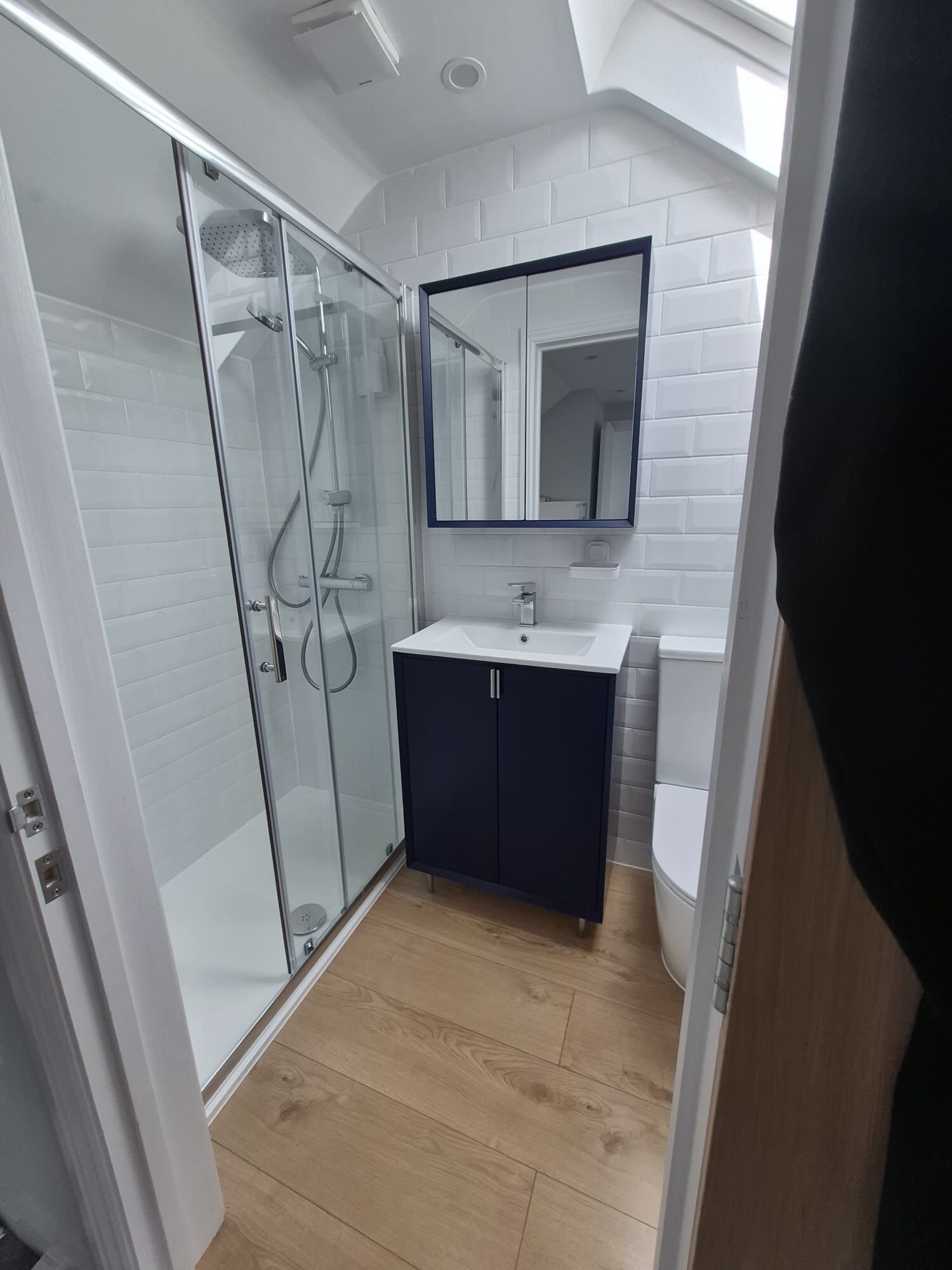 A modern bathroom with a glass shower enclosure, a dark vanity, and a white sink.