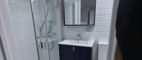 Een moderne badkamer met een douchecabine van glas, een donkere wastafel en een witte wasbak.