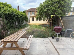A wooden picnic table in a backyard with a barbecue grill and a wheelbarrow. - West London 3-bed 3 bath family house, a/c in charming neighbourhood near centre (London)