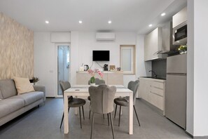 Un espace de vie moderne comprenant un coin repas, un canapé, une cuisine avec un four encastré et un téléviseur à écran plat.