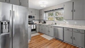 Une cuisine moderne dotée d’appareils électroménagers en acier inoxydable, de meubles de rangement gris et d’une fenêtre avec des stores.