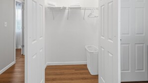Un dressing accessible sans porte, avec un plancher en bois, des portes blanches et une étagère suspendue pour ranger les vêtements.