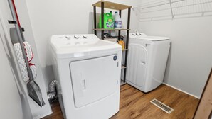 Une buanderie équipée d’un lave-linge, d’un sèche-linge et d’étagères où sont rangés les produits de nettoyage.