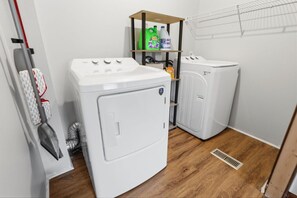 Une buanderie équipée d’un lave-linge, d’un sèche-linge et d’étagères où sont rangés les produits de nettoyage.