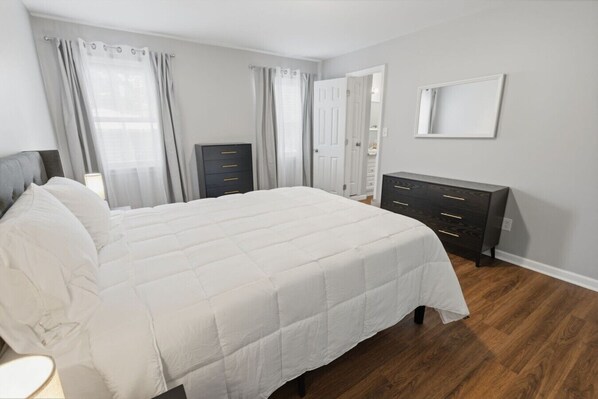 Une chambre à coucher avec un grand lit, une commode, un miroir et une porte.