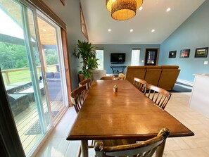 Un coin repas avec une longue table en bois, des chaises, une plante en pot et un téléviseur fixé au mur.