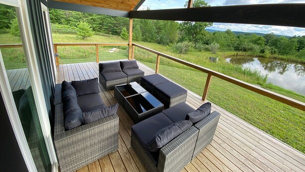 En overdækket terrasse med fletmøbler og udsigt til en sø.