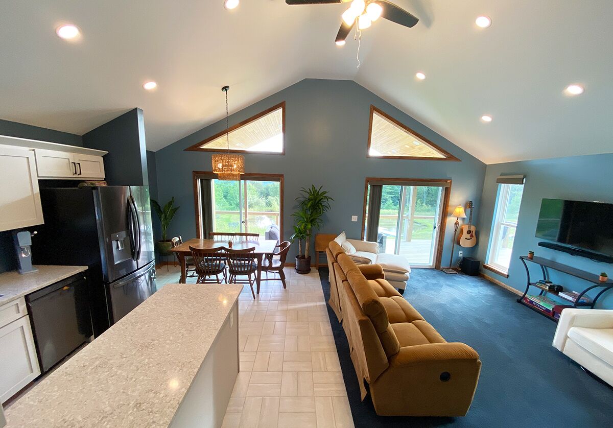 A modern kitchen with a dining area, a living room with a sofa, and a TV.