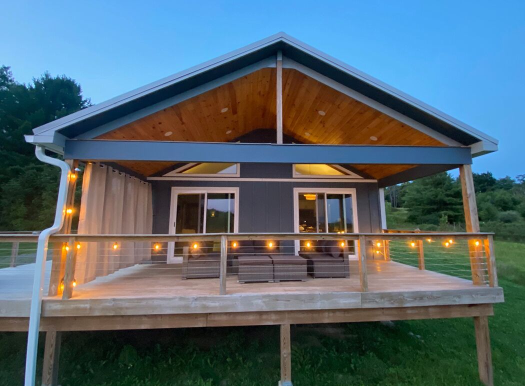 A modern house with a covered porch, large windows, and a deck with seating.