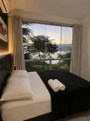 A hotel room with a large window, a bed with white linens, and a black bedspread. - House in Mirante with Panoramic Sea View (Angra dos Reis)