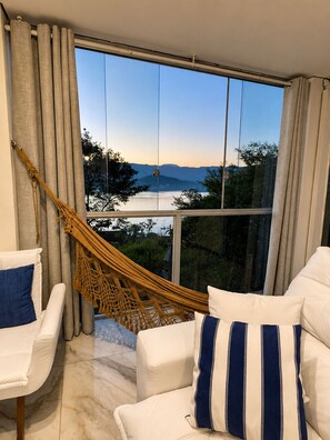 A room with a large window, a hammock, and two white chairs with pillows. - House in Mirante with a panoramic view of the sea (Angra dos Reis)