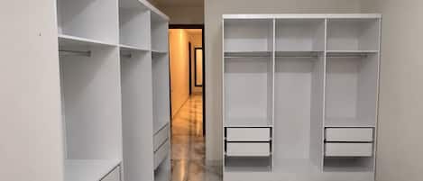 Ein begehbarer Kleiderschrank mit offenen Regalen und Schubladen, Marmorboden und einem Gang zu einem weiteren Zimmer.