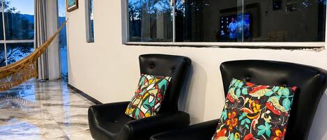 A modern living room with two black leather chairs, a small black ottoman, and a hammock.