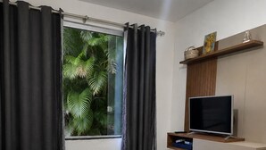 Ett sovrum med två sängar, en tv och ett fönster med gardiner.