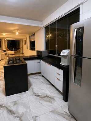 A modern kitchen with a central island, black countertop, white cabinets, and a stainless steel refrigerator. - House in Mirante with a panoramic view of the sea (Angra dos Reis)