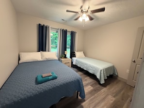 A bedroom with two beds, a ceiling fan, and a window with curtains.