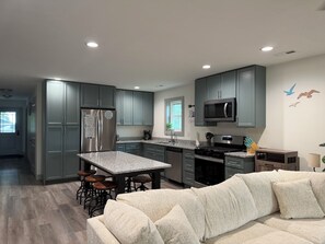 A modern kitchen with grey cabinets, a stainless steel refrigerator, a microwave, and a dining area with stools.