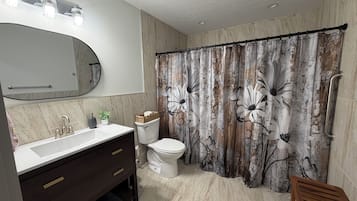 Une salle de bain avec un lavabo blanc, un meuble-lavabo en bois foncé, des toilettes blanches et un rideau de douche orné de motifs floraux.