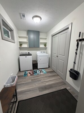 A laundry room with a washing machine, dryer, and a broom leaning against the wall.