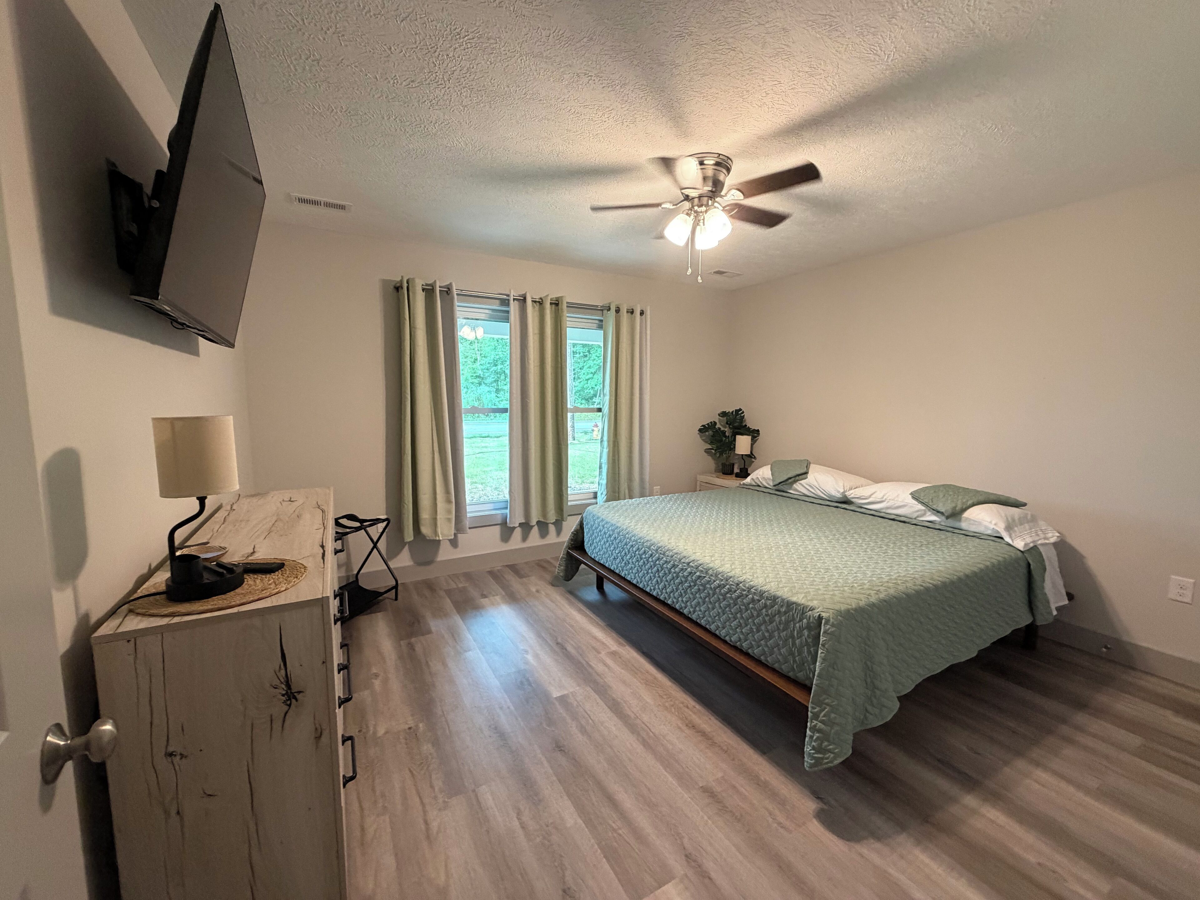 A bedroom with a bed, a desk, a ceiling fan, and a window with curtains.