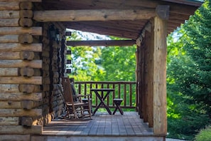 Eine Holzblockhütte mit Veranda, Sitzgelegenheiten im Freien und Blick ins Grün.