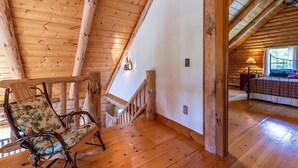 A wooden interior with a sloped ceiling, a staircase, and a bed with a patterned bedspread. - Log Cabin Retreat on Private Vermont Estate (Reading)
