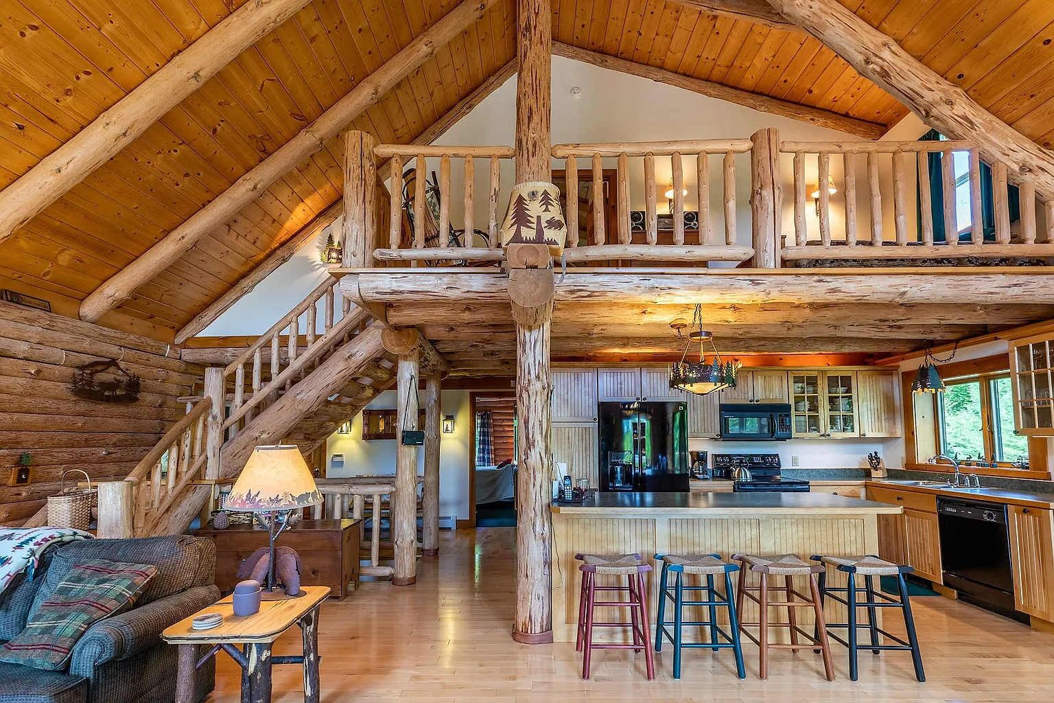 Un intérieur spacieux de chalet en bois, avec un plafond haut, un escalier central, un coin cuisine et un espace salon confortable.