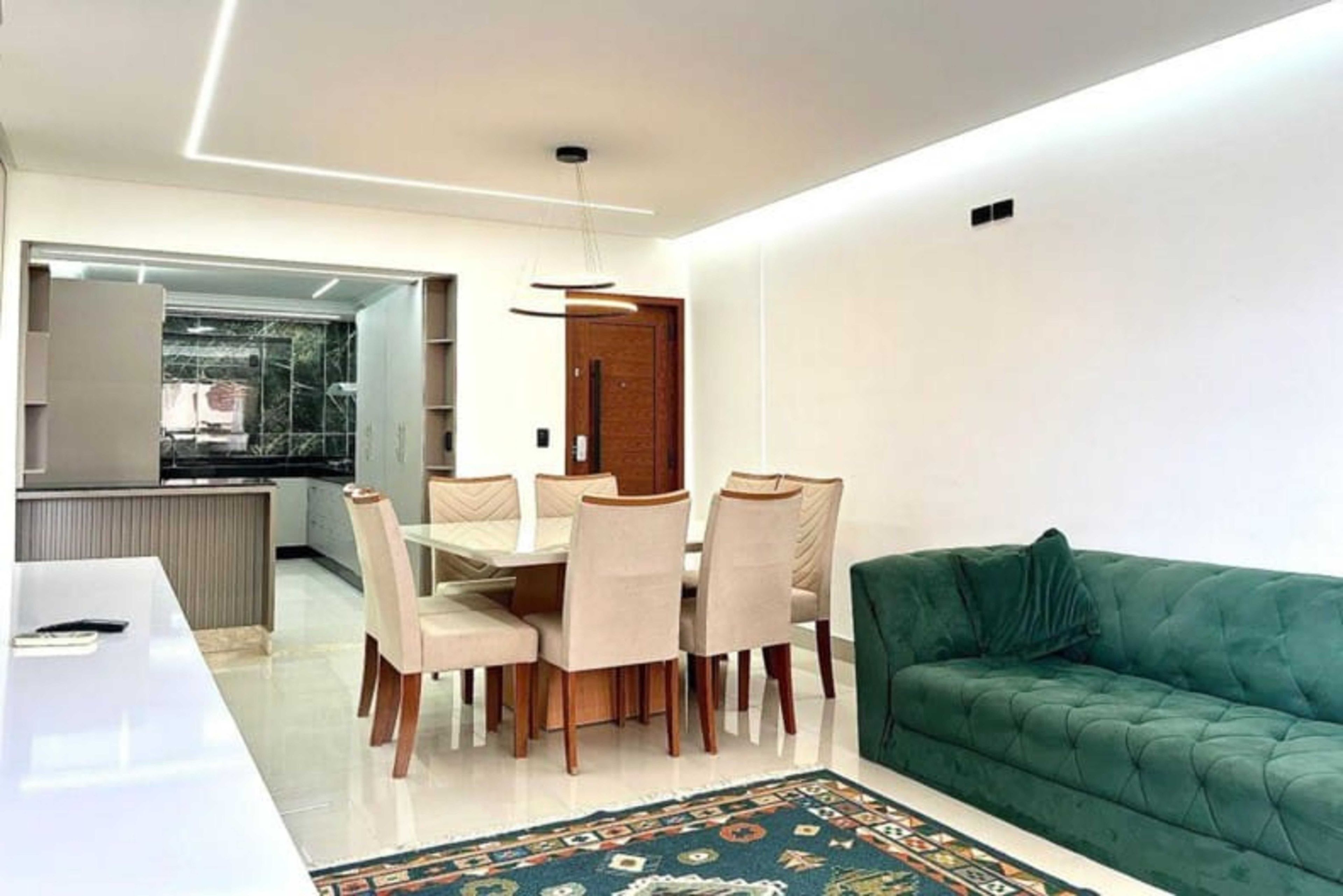 A modern living room with a dining area, a green sofa, and a patterned rug.