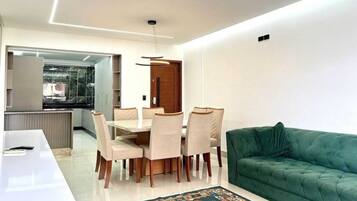 A modern living room with a dining area, a green sofa, and a patterned rug.