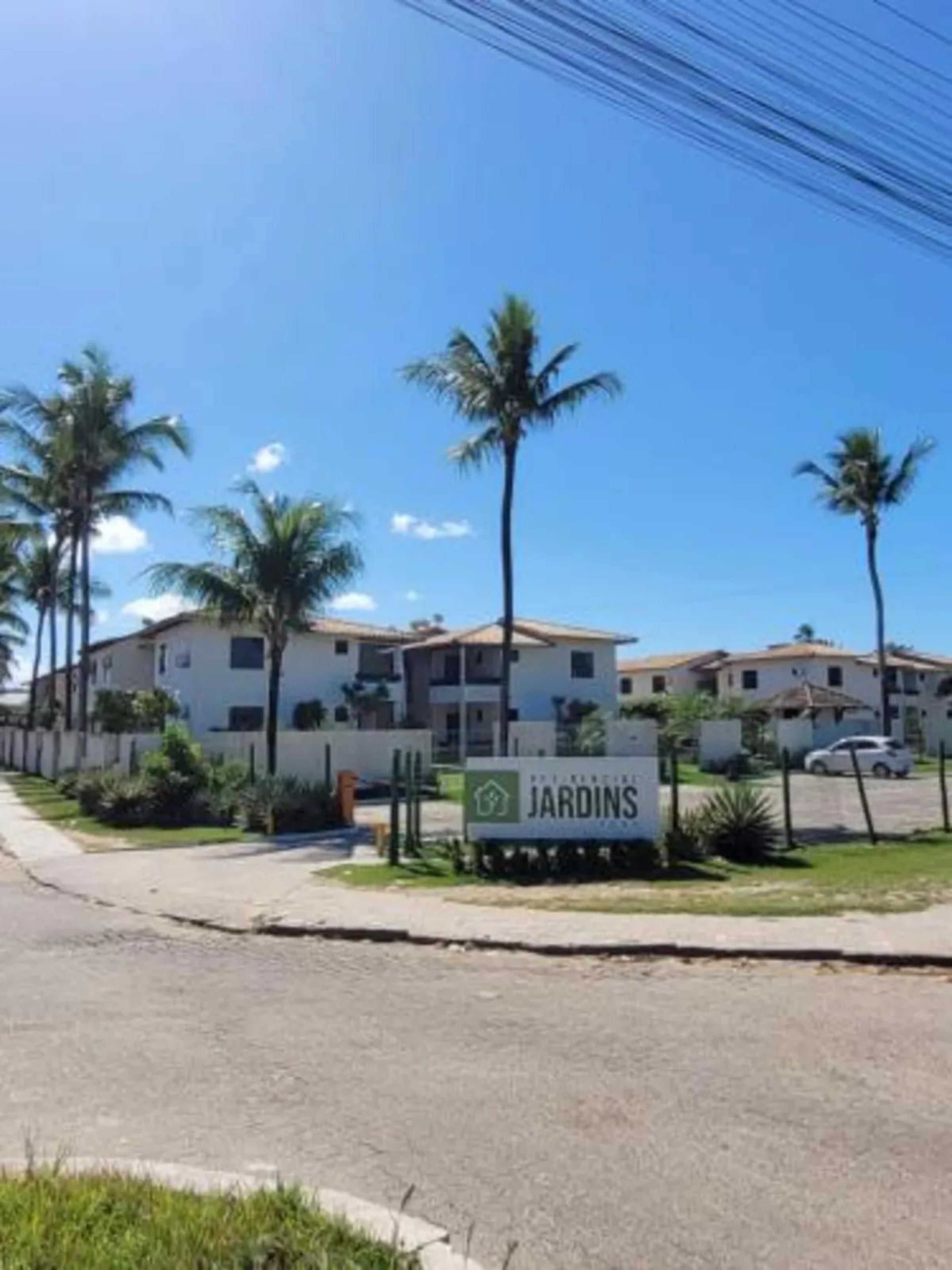 A residential complex with multiple two-story buildings, a sign reading 'JARDINS,' and a parking area with a few cars.