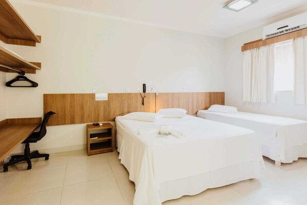 Habitación de hotel con escritorio, dos camas, una silla, una mesita y ventana con cortinas.