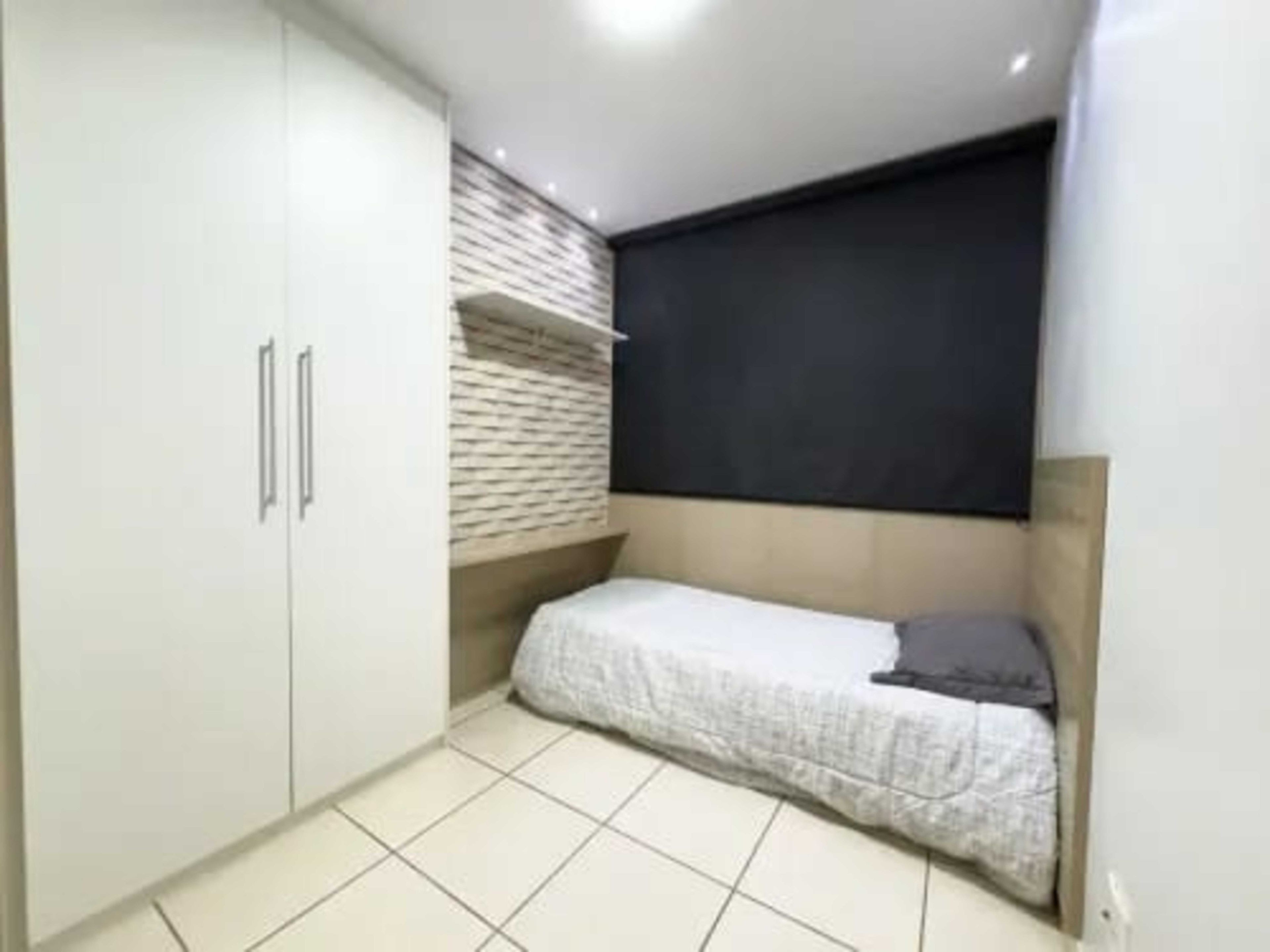 Quarto pequeno e funcional, com cama, guarda-roupa e prateleira na parede.