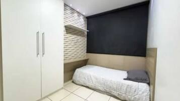 Quarto pequeno e funcional, com cama, guarda-roupa e prateleira na parede.