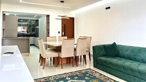 A modern living room with a green sofa, a dining table with chairs, and a kitchen area visible through an open door. - Residencial Jardins Taperapuan (Porto Seguro)