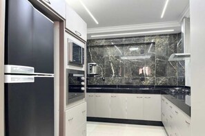 A modern kitchen with a black countertop, white cabinets, and a marble backsplash. - Residencial Jardins Taperapuan (Porto Seguro)
